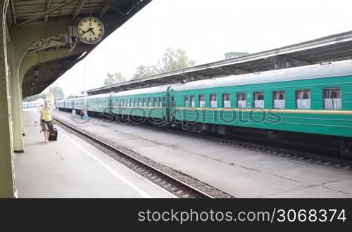 Woman with trolley case walking along platform at the railway station. Passenger train in background.