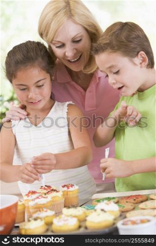 Woman with two children in kitchen decorating cookies smiling