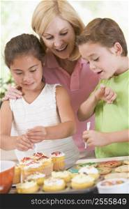 Woman with two children in kitchen decorating cookies smiling