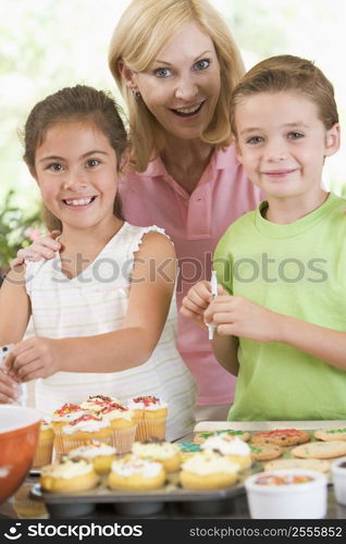 Woman with two children in kitchen decorating cookies smiling