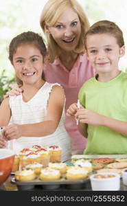 Woman with two children in kitchen decorating cookies smiling