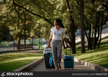 Woman with two suitcases on walkway in summer park. Female traveler with luggage leisures outdoors, passenger with bag resting in nature. Girl with baggage relax on city alley. Woman with two suitcases on walkway in summer park