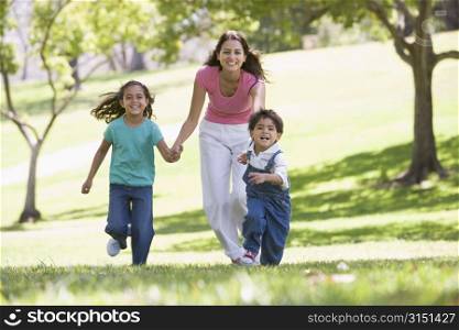 Woman with two young children running outdoors smiling