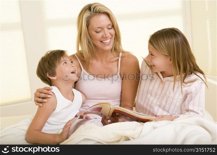Woman with two young children sitting in bed reading book and smiling