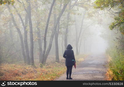 Woman with umbrella on road and foggy forest