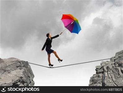 Woman with umbrella. Young businesswoman walking on rope above gap with colorful umbrella