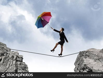 Woman with umbrella. Young businesswoman walking on rope above gap with colorful umbrella