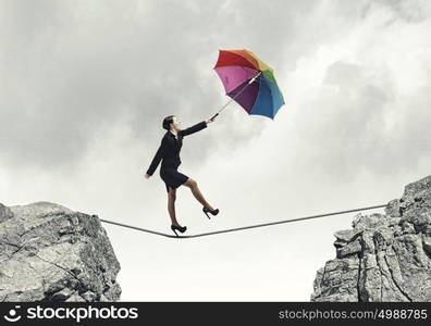 Woman with umbrella. Young businesswoman walking on rope above gap with colorful umbrella