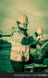 Woman worker on the oil field repairing of oil and gas well, with the wrench wearing helmet and work clothes. Working process on oil wellhead. Toned sepia.
