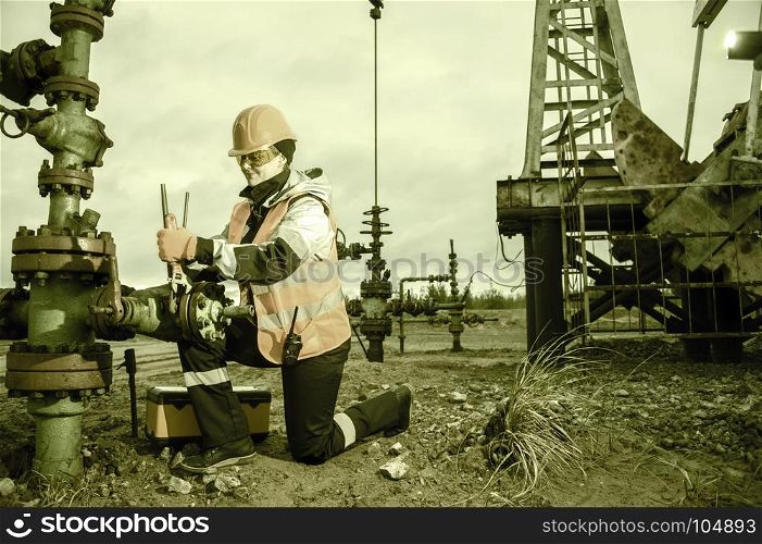 Woman worker on the oil field repairing of oil and gas well, with the wrench wearing helmet and work clothes. Working process on oil wellhead.