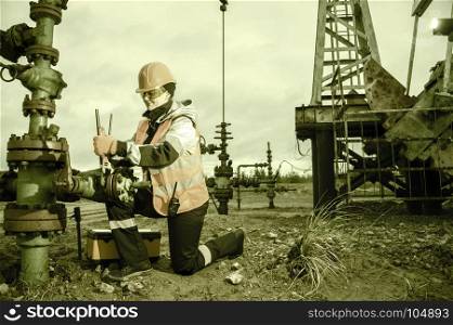 Woman worker on the oil field repairing of oil and gas well, with the wrench wearing helmet and work clothes. Working process on oil wellhead.