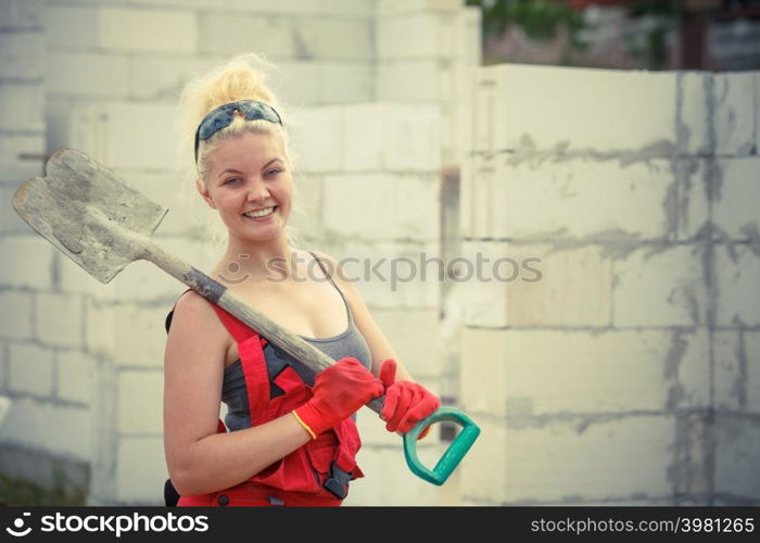 Woman worker using shovel standing on industrial construction site, working hard on house renovation.. Person using shovel on construction site