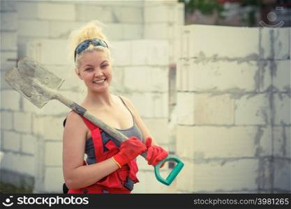 Woman worker using shovel standing on industrial construction site, working hard on house renovation.. Person using shovel on construction site