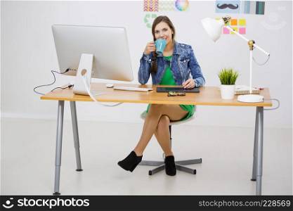 Woman working at desk, in a creative office and drinking a coffee