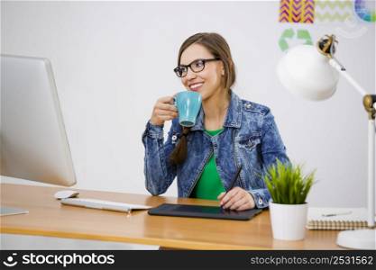 Woman working at desk, in a creative office and drinking a coffee