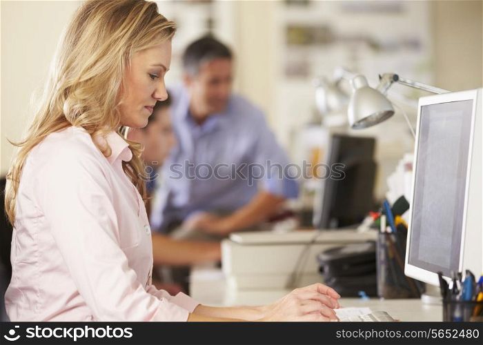 Woman Working At Desk In Busy Creative Office