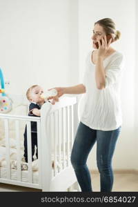 Woman working at home and talking by phone while feeding her baby