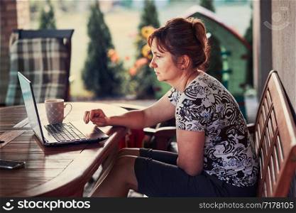 Woman working at home, using portable computer, sitting on patio on summer day. Candid people, real moments, authentic situations
