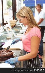 Woman Working Behind Counter In Cafe Slicing Cake