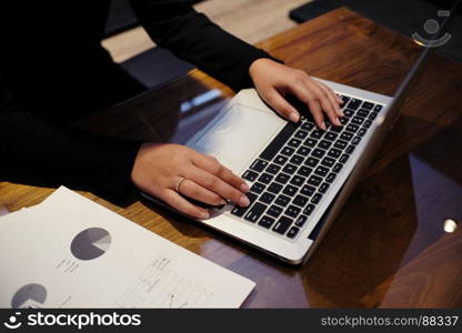 Woman working by using a laptop computer on wooden table. Hands typing on a keyboard.