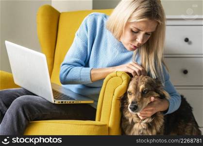 woman working laptop from armchair during pandemic petting her dog