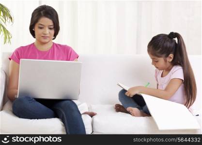 Woman working on laptop while daughter drawing