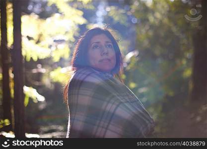 Woman wrapped in checkered shawl in forest