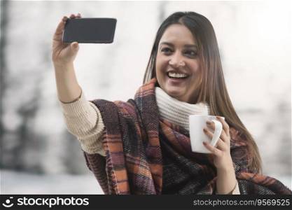 Woman wrapped in shawl talking on a videocall with a coffee mug in her hand