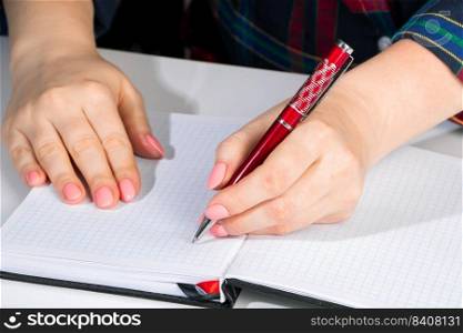 Woman writes in a notebook and holds a pen with her left hand. The girl works in the office. Left-handers Day August 13th.. Woman writes in a notebook and holds pen with her left hand. The girl works in the office. Left-handers Day August 13th.