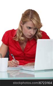 Woman writing notes from laptop