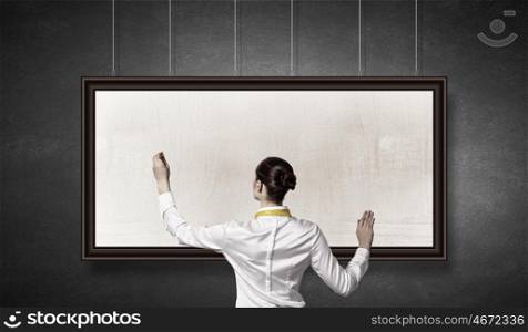 Woman writing on billboard. Rear view of businesswoman drawing on white blank banner on wall