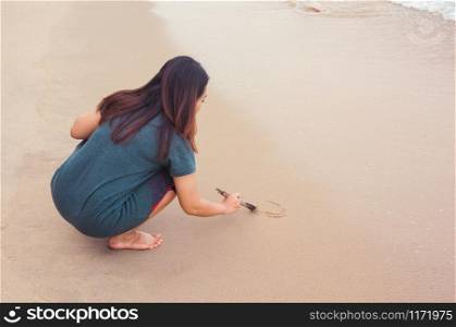 Woman writing on sandy beach with tree branch
