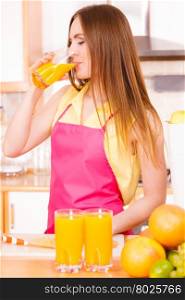 Woman young housewife in kitchen at home drinking fresh homemade orange juice drink. Healthy eating, vegetarian food, weight loss and people concept.