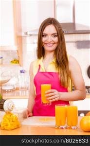 Woman young housewife in kitchen at home drinking fresh homemade orange juice drink. Healthy eating, vegetarian food, weight loss and people concept.