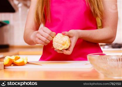 Woman young housewife in kitchen at home peeling orange fruit for salad or juicing. Healthy eating, cooking, raw food, dieting and people concept.. Woman hands peeled orange fruit closeup