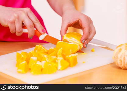 Woman young housewife in kitchen at home slicing fresh orange fruits on cutting board for salad or juicing. Healthy eating, cooking, raw food, dieting and people concept.. Woman housewife in kitchen cutting orange fruits