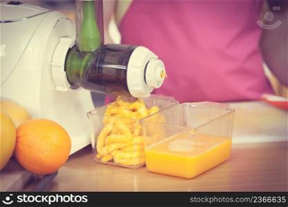 Woman young housewife in kitchen making fresh orange juice in juicer machine, preparing nutritious vitamin packed drink. Healthy eating, vegetarian food, dieting and people concept. Woman making orange juice in juicer machine
