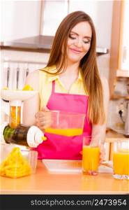 Woman young housewife in kitchen making fresh orange juice in juicer machine, pouring drink from jug in glass. Healthy eating, vegetarian food, dieting and people concept. . Woman make orange juice in juicer machine pouring drink in glass