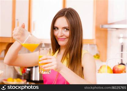 Woman young housewife in kitchen making fresh orange juice in juicer machine, pouring drink from jug in glass. Healthy eating, vegetarian food, dieting and people concept.