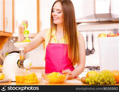 Woman young housewife in kitchen making fresh orange juice in juicer machine, preparing nutritious vitamin packed drink. Healthy eating, vegetarian food, dieting and people concept