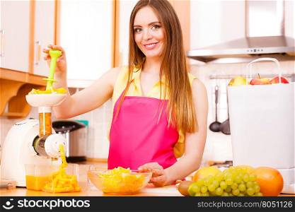 Woman young housewife in kitchen making fresh orange juice in juicer machine, preparing nutritious vitamin packed drink. Healthy eating, vegetarian food, dieting and people concept