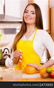 Woman young housewife in kitchen with fruits and juicer preparing to make fresh juice, cutting with knife grapefruit. Healthy eating, cooking, vegetarian food, dieting and people concept.. Woman in kitchen preparing fruits for juicing