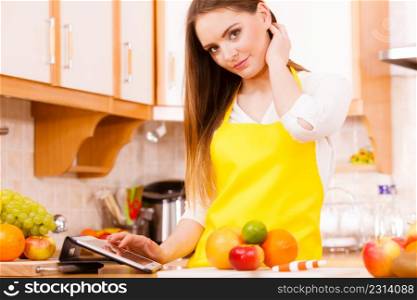 Woman young housewife in kitchen with many fruits on counter using tablet looking at recipes. Healthy eating, cooking, vegetarian food, dieting and technology concept.. Woman housewife in kitchen using tablet