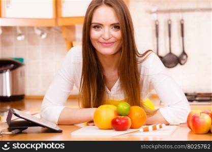 Woman young housewife in kitchen with many fruits on counter using tablet looking at recipes. Healthy eating, cooking, vegetarian food, dieting and technology concept.