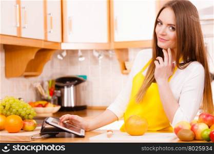 Woman young housewife in kitchen with many fruits on counter using tablet looking at recipes. Healthy eating, cooking, vegetarian food, dieting and technology concept.