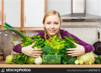 Woman young positive housewife in kitchen with many green leafy vegetables, fresh produce organically grown on counter. Healthy lifestyle, cooking, vegetarian food, dieting and people concept.. Smiling woman in kitchen with green vegetables