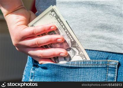 Womana??s hand is putting dollar money in jeans pocket. Womana??s hand is putting money in pocket