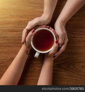 Womans and mens hands holding hot cup of tea on wooden table