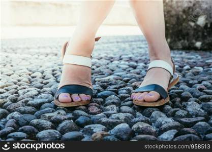 Womans legs wearing sandals on the pavement, summertime.