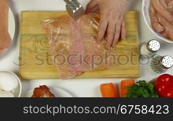 Women&acute;s hands tenderizing chicken breast. Shoot from above